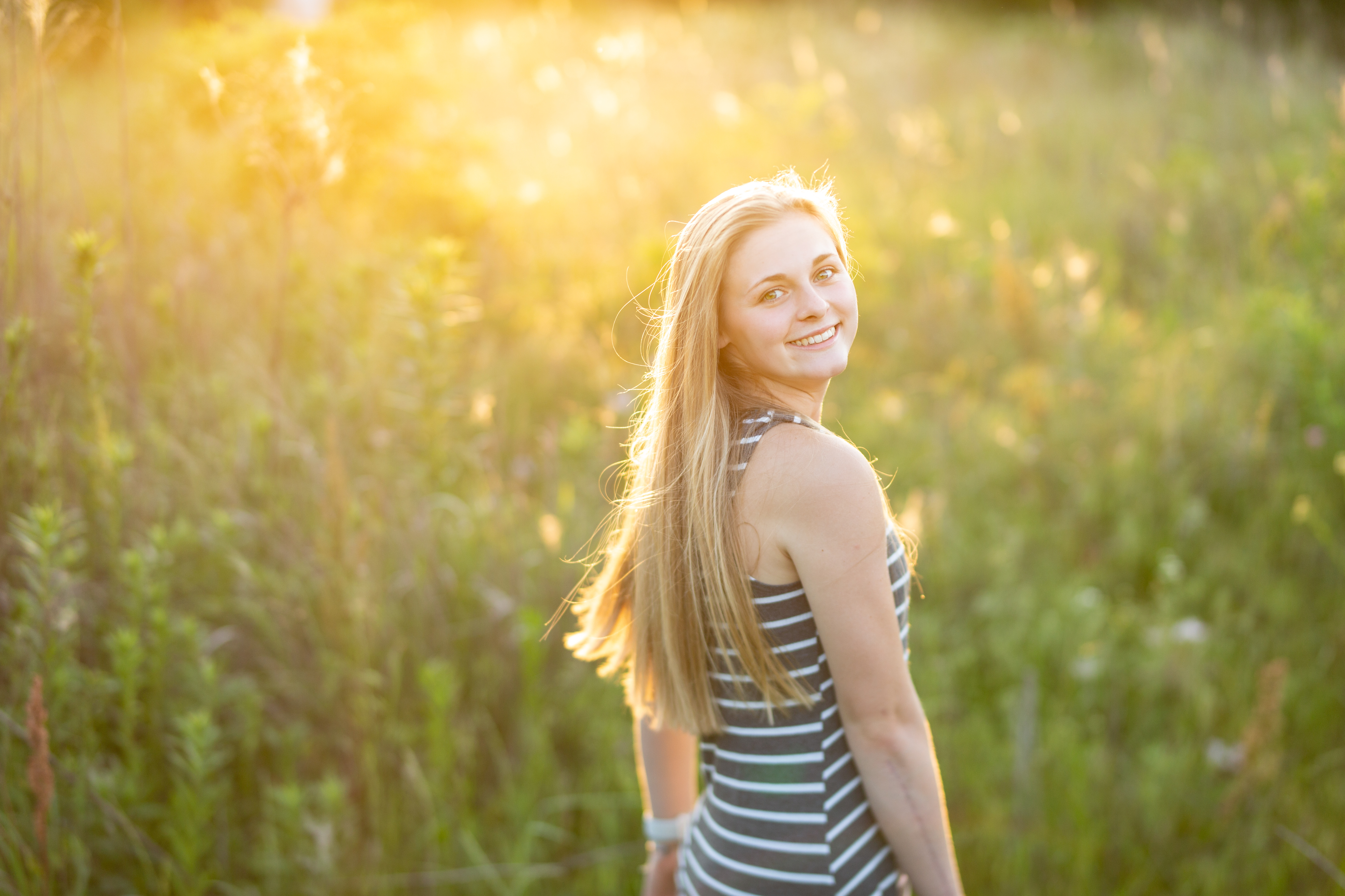 senior girl posing in a field during golden hour