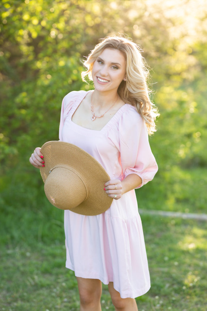 senior girl posing in a field with a hat for her senior photos