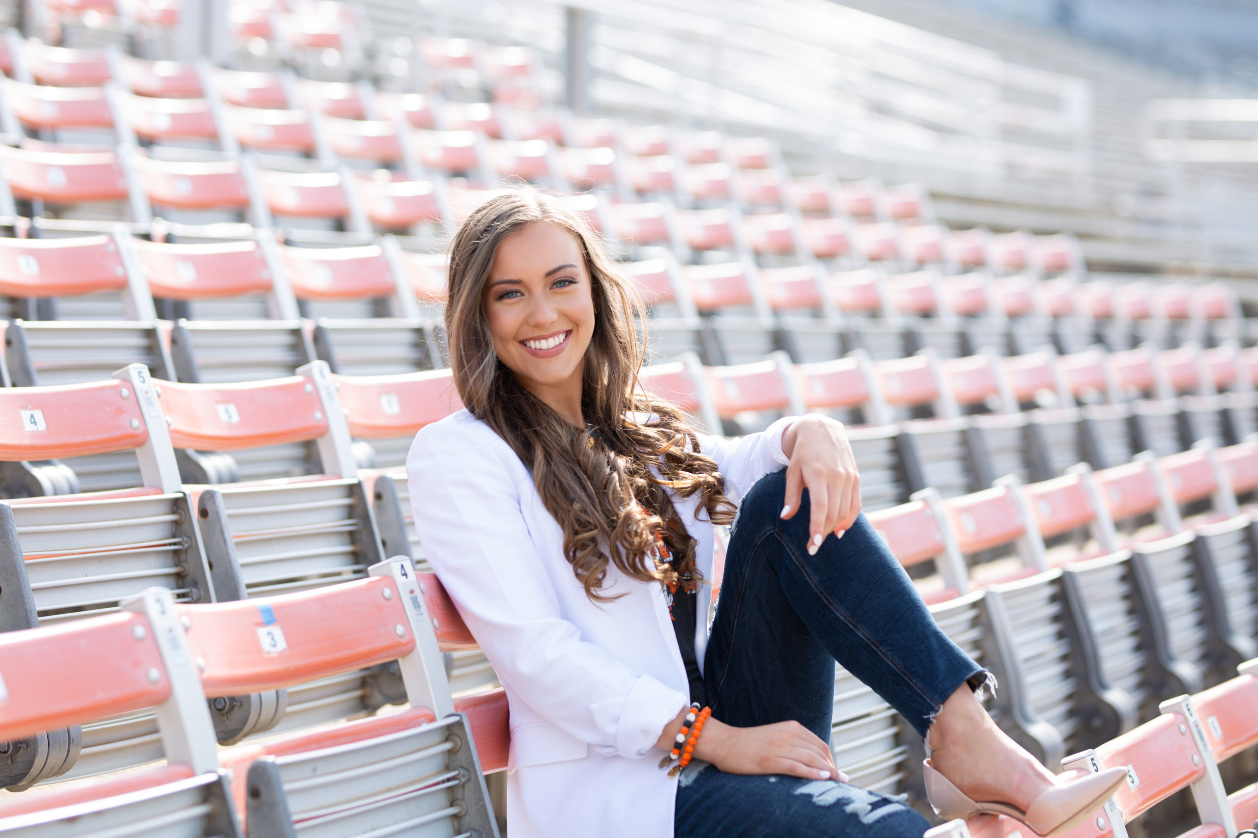 senior girl sitting in stands at Boone Pickens Stadium on the campus of OSU for her senior photos