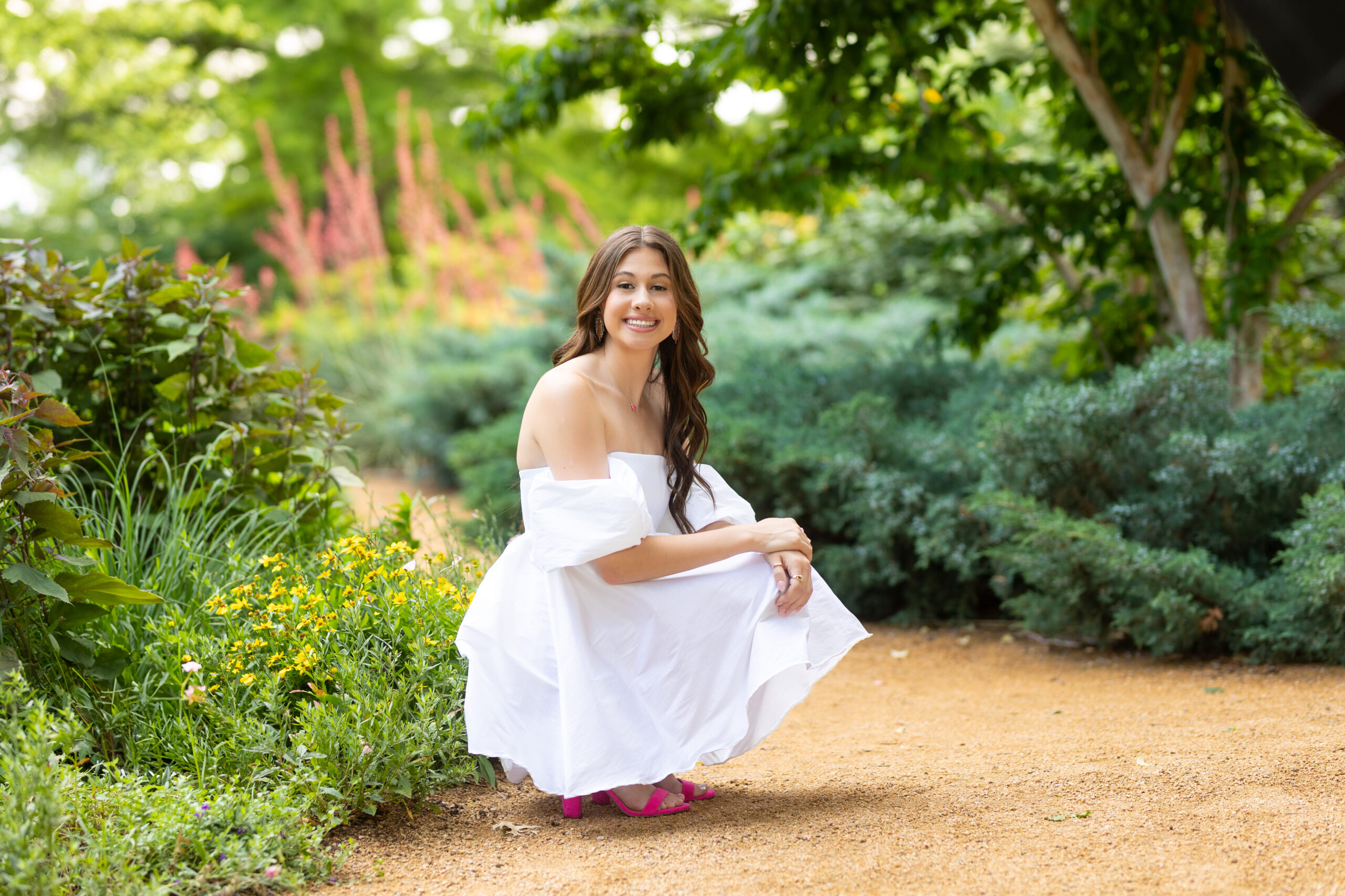 senior girl posing in a flower garden for her senior pictures wearing a white dress