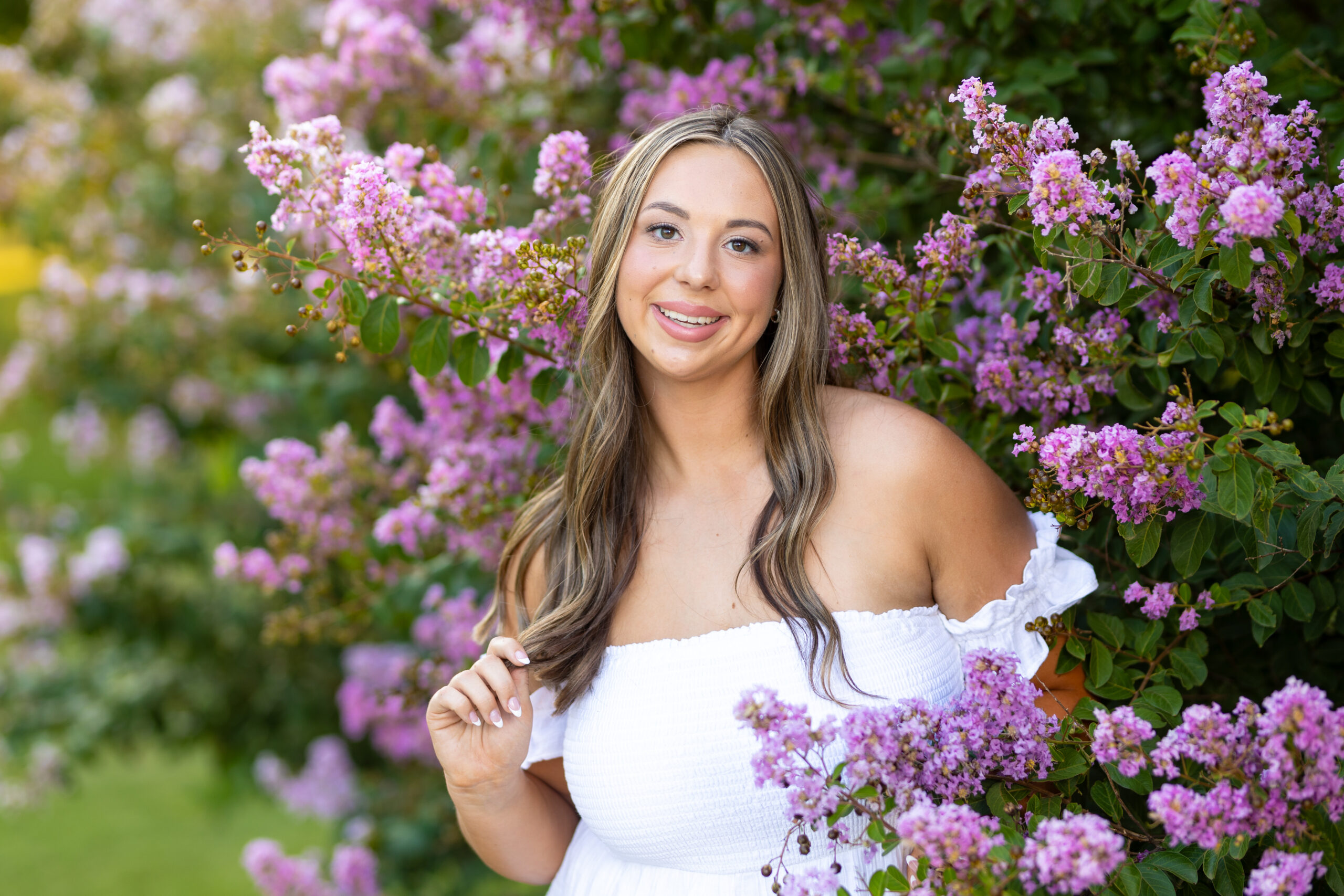 senior girl posing in purple flowers for her summer senior pictures in a white flowy dress