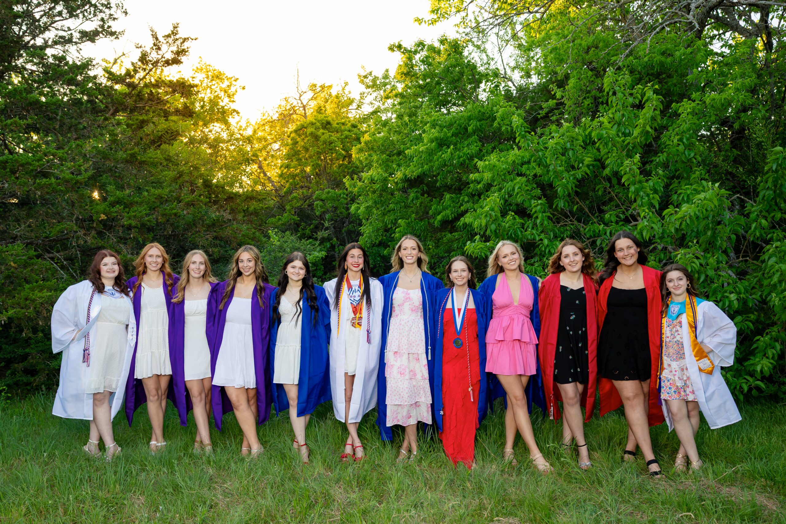 group of senior girls in their cap and gowns posing for pictures in a nature park