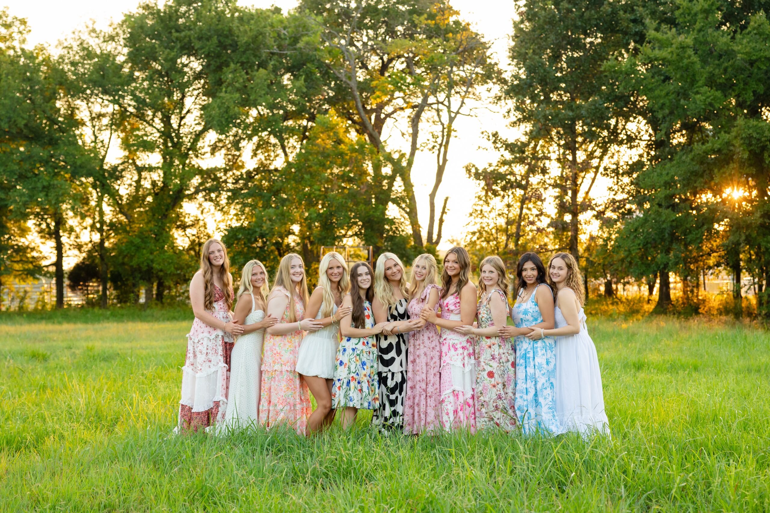 a group of high school senior girls posing together in a field in flowy dresses