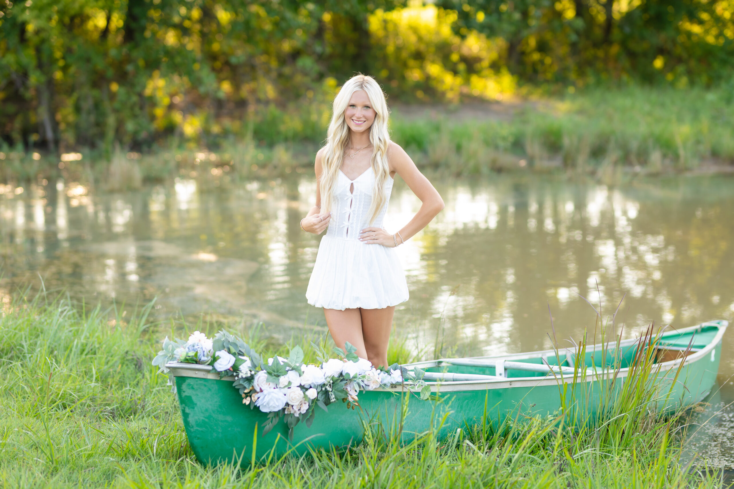 senior girl posing in a white dress in a canoe in oklahoma for her senior photos
