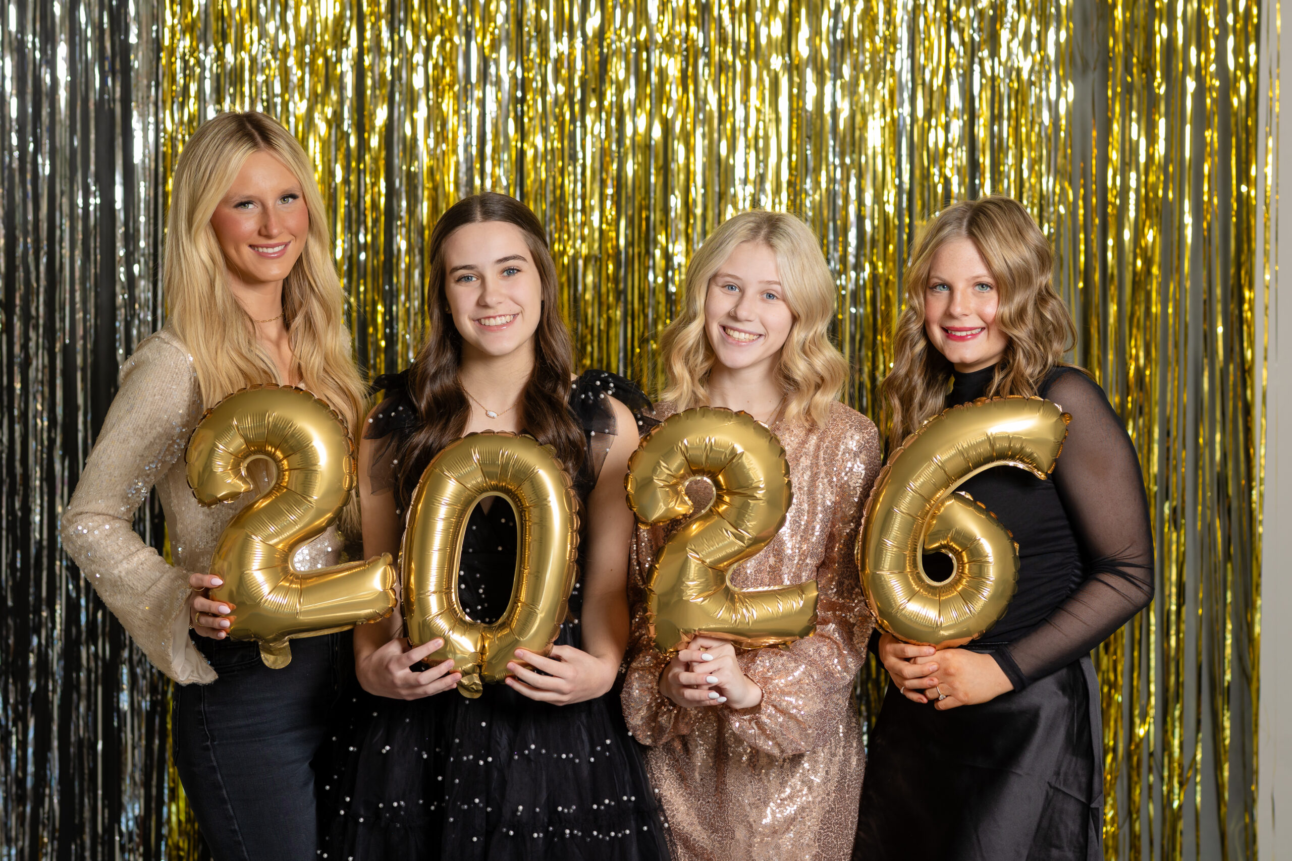 a group of senior girls posing in a studio with gold and silver decorations for a new year's eve session during their senior year of high school
